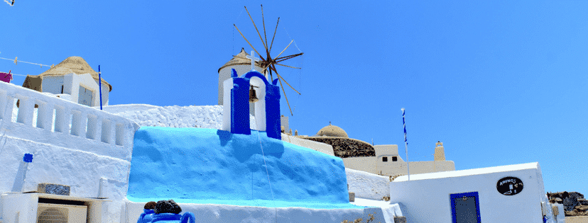 photo of a windmill in greece atop beautiful greek architecture and the beautiful greek landscape