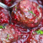 Savoury cranberry meatball getting served on a silver spoon.