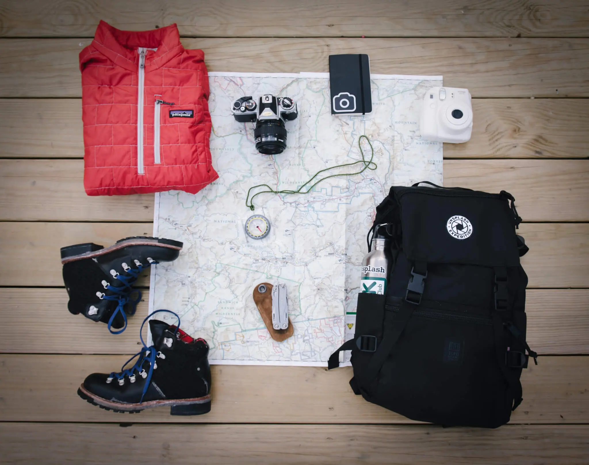 A flatlay with a travel backpack and other travel accessories like a compass and map.