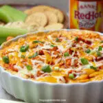 Franks buffalo chicken dip in a serving bowl next to celery, ritz crackers, and other dippers.