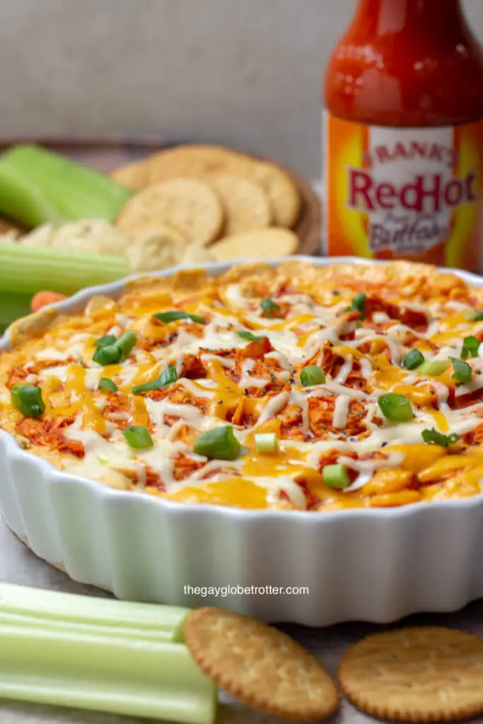 Franks buffalo chicken dip in a serving bowl next to celery, ritz crackers, and other dippers.