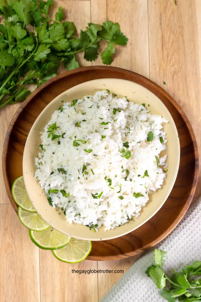 A bowl of cilantro lime rice surrounded by limes and cilantro.