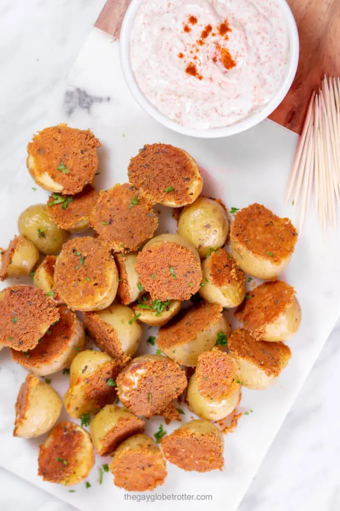 A platter of crispy parmesan roasted potatoes next to some chili sour cream dip and toothpicks.