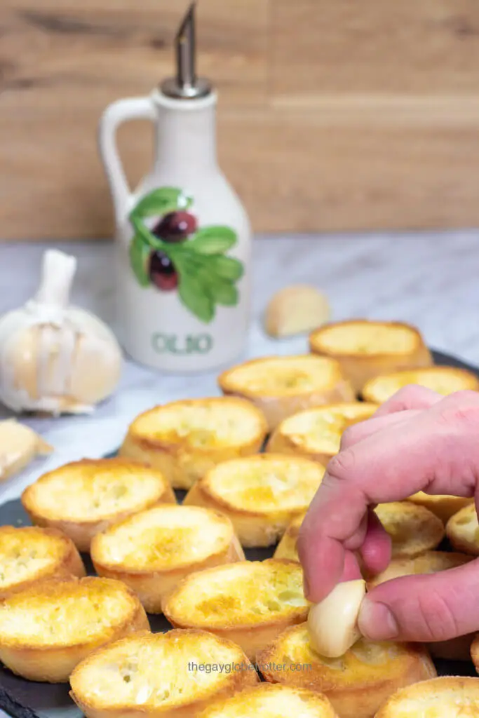 A hand rubbing fresh garlic onto fresh crostini.