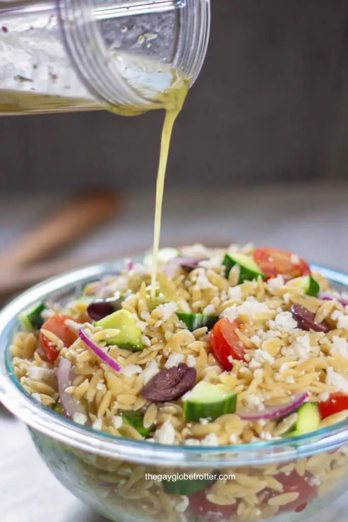 Greek lemon dressing being poured into a bowl of Greek pasta salad.