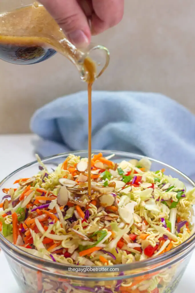 A serving bowl of ramen noodle salad with Asian sesame dressing being poured into it.