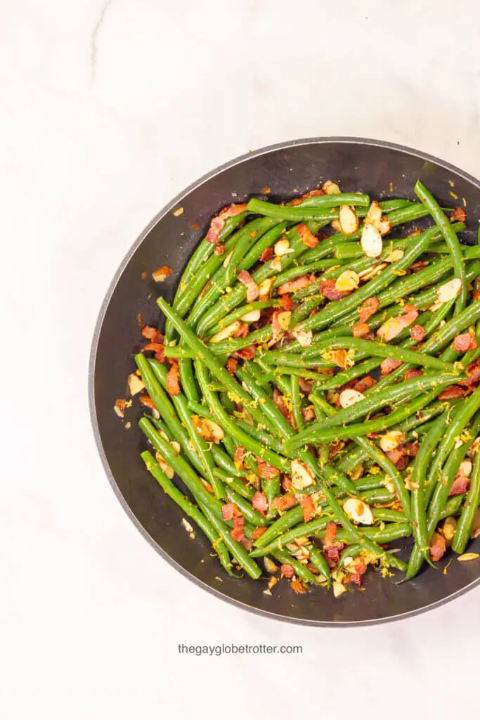 A sauce pan filled with green beans, almonds, and bacon.