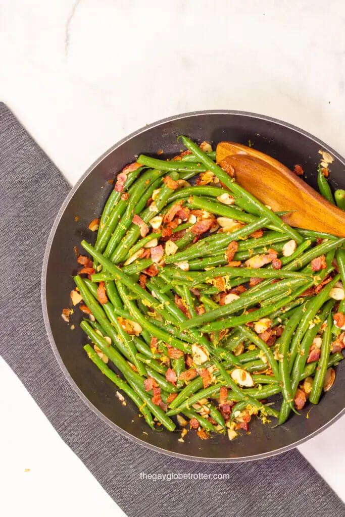 A pan full of green beans almondine with a wooden spoon.