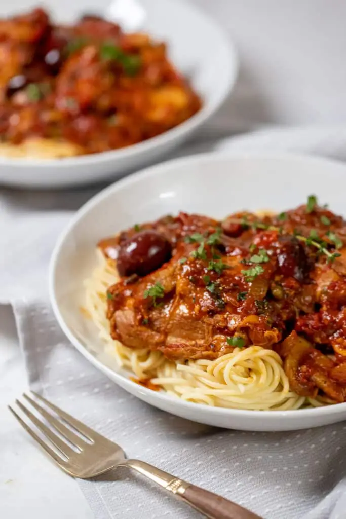 A bowl of chicken cacciatore over spaghetti noodles.