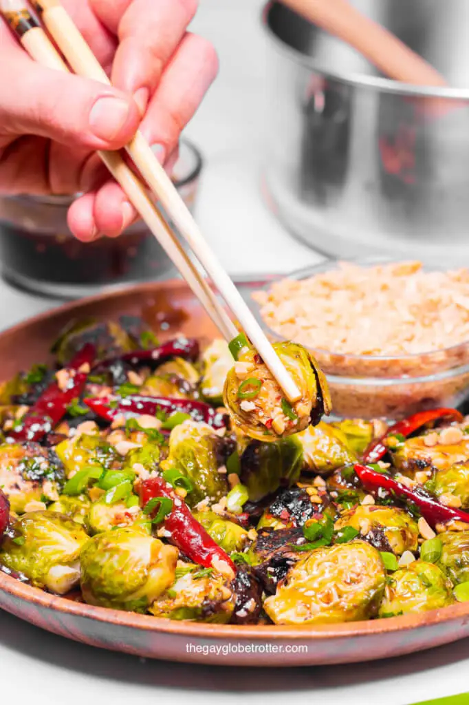 A hand grabbing kung pao brussels sprouts with chopsticks. 