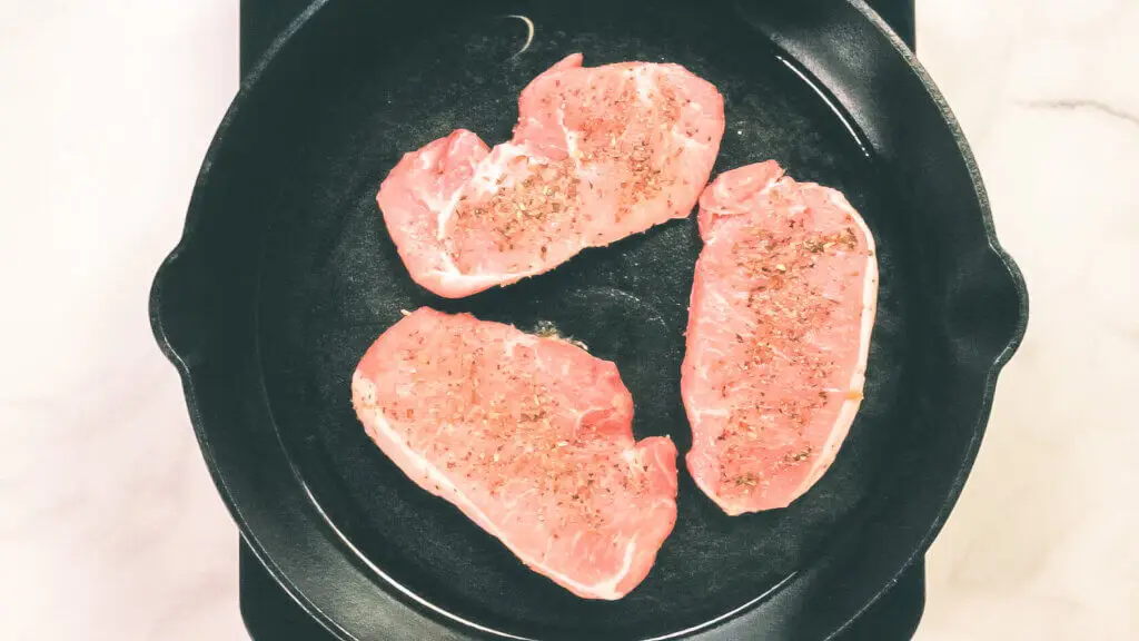 A process shot of pork chops being seared in a cast iron pan.