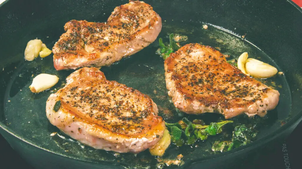 Pan seared pork chops in a pan with oregano and garlic.