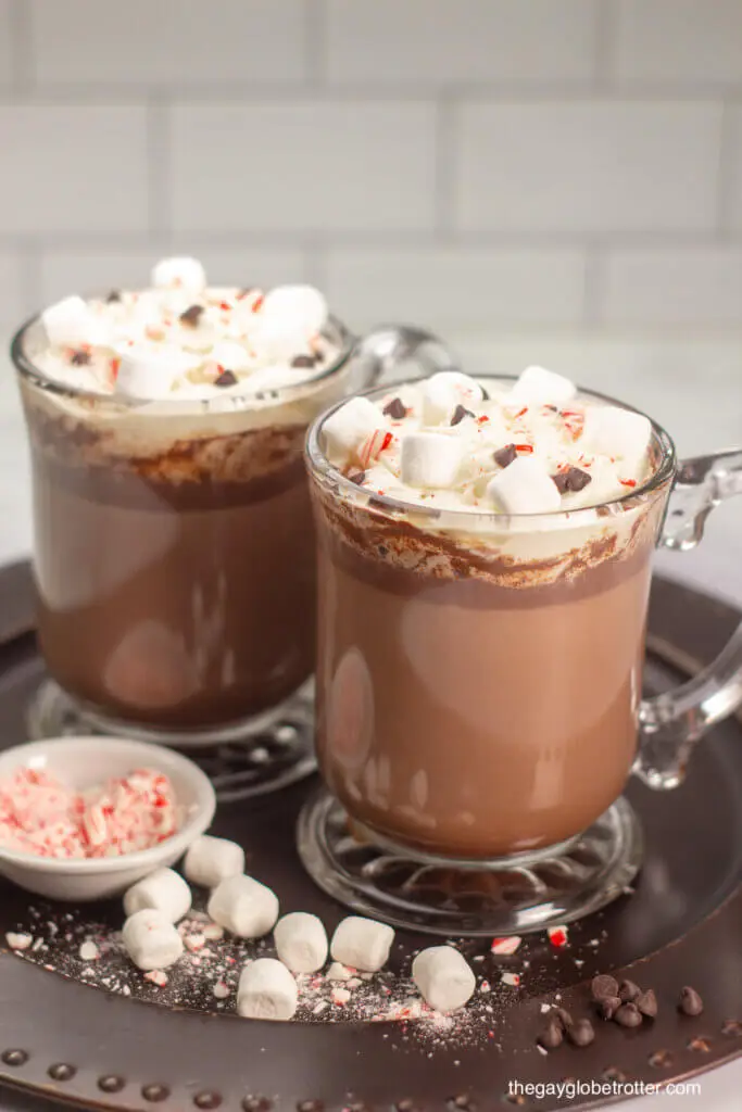 Two cups of homemade hot chocolate on a serving tray with marshmallows and candy cane pieces.