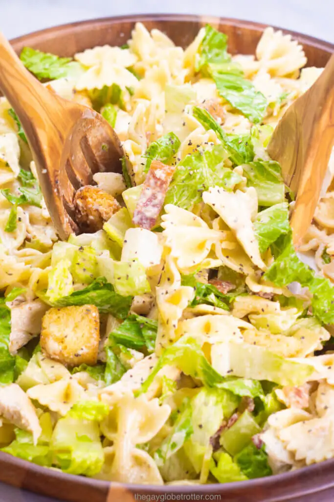 Wooden salad spoons tossing caesar pasta salad. together in a serving bowl.