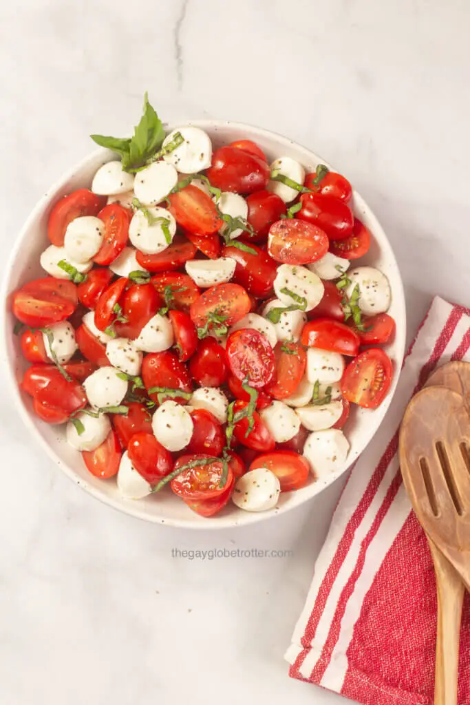 Caprese salad next to serving spoons on a cloth napkin.