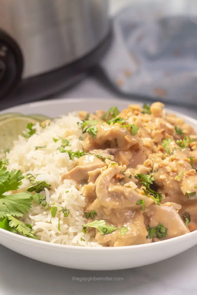 A bowl of thai peanut chicken served over coconut rice with limes and cilantro. 