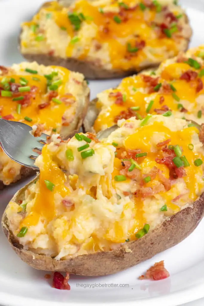 A fork picking up some of a twice baked potato topped with cheese and chives.