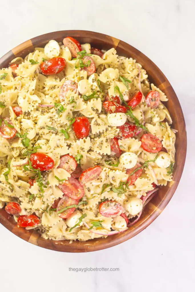 A wooden serving bowl of caprese pesto pasta salad with tomatoes, basil, and bocconcini.