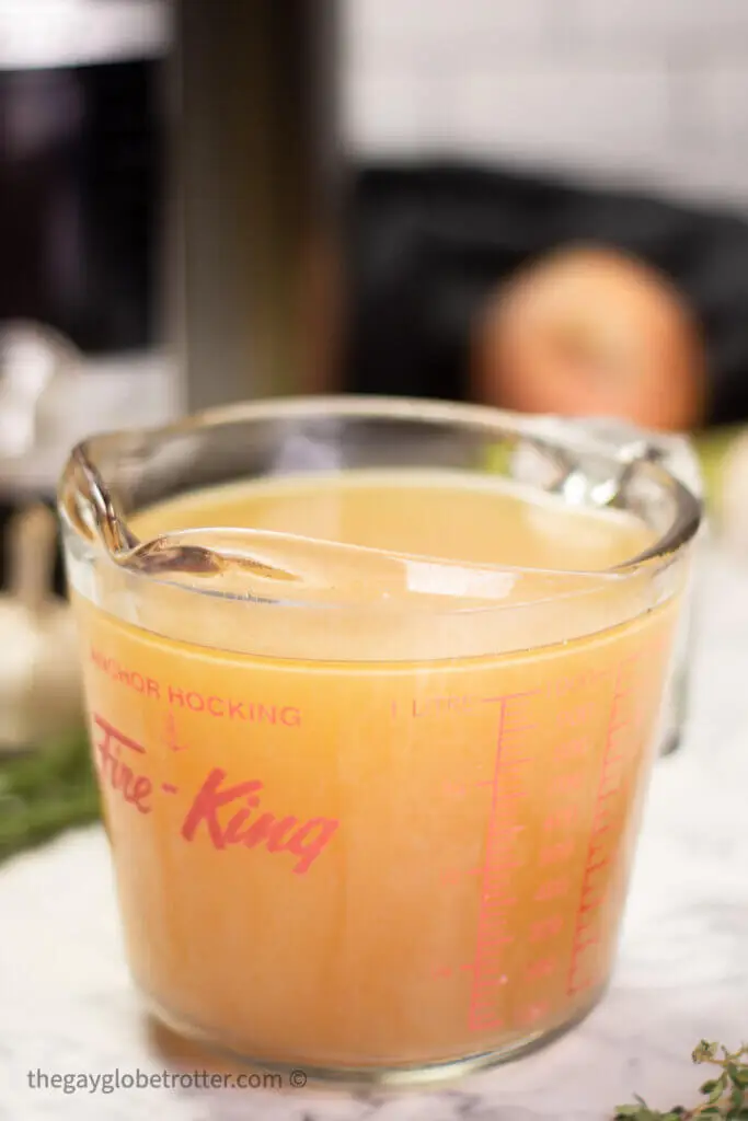 A measuring cup of Instant pot turkey stock with an Instant Pot behind it.