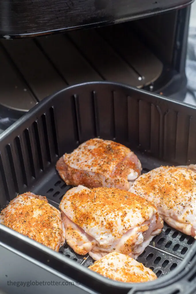 Uncooked chicken thighs seasoned in the air fryer basket.