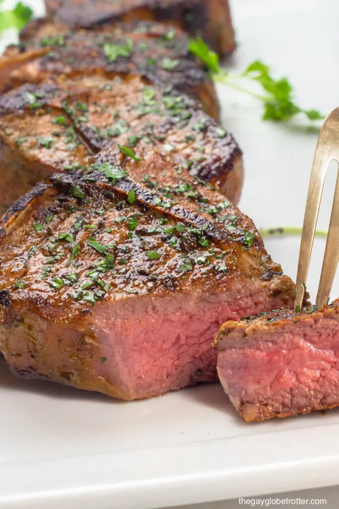 A fork cutting into a lamb loin chop to show it is cooked medium rare.