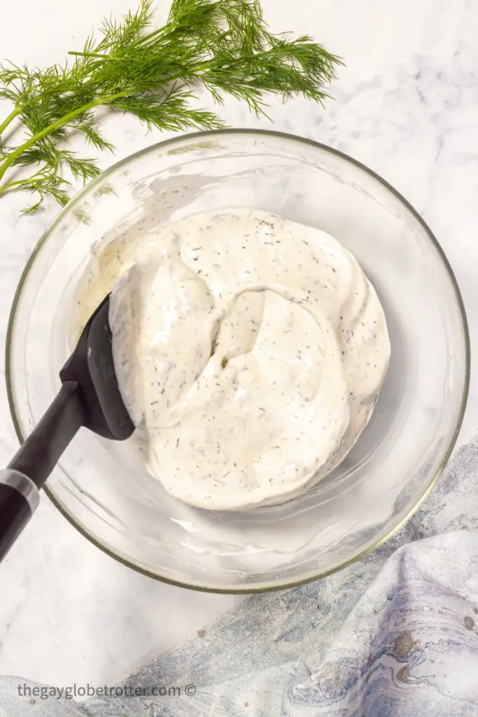 A spatula mixing dill dip in a mixing bowl.