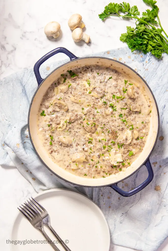 A pot of ground beef stroganoff with a tea towel and mushrooms.