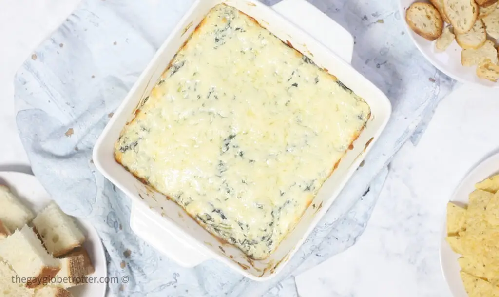 Hot spinach artichoke dip in a baking dish next to crostini.