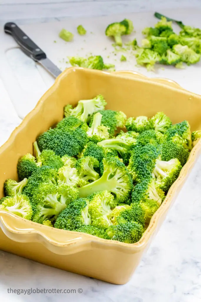 Broccoli florets being cut and placed in a baking dish.