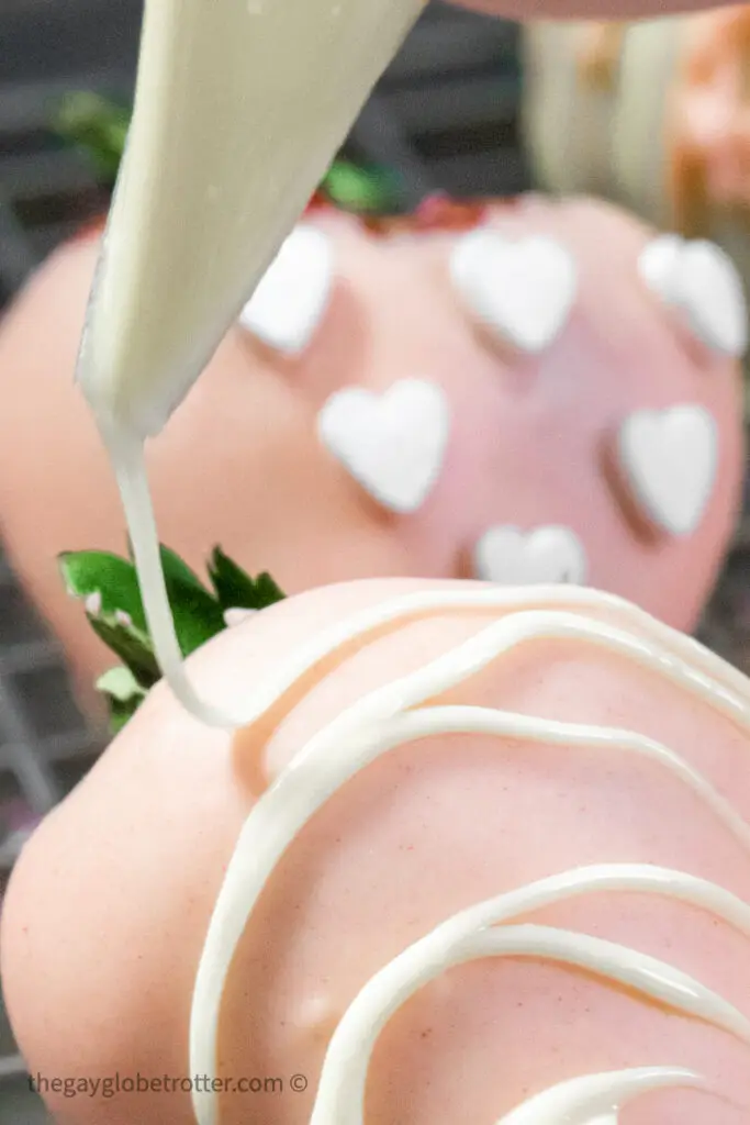 A pink chocolate covered strawberry being decorated with a piping bag.