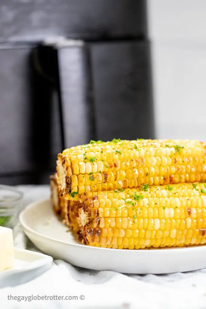 Corn on the cob on a plate next to an air fryer.