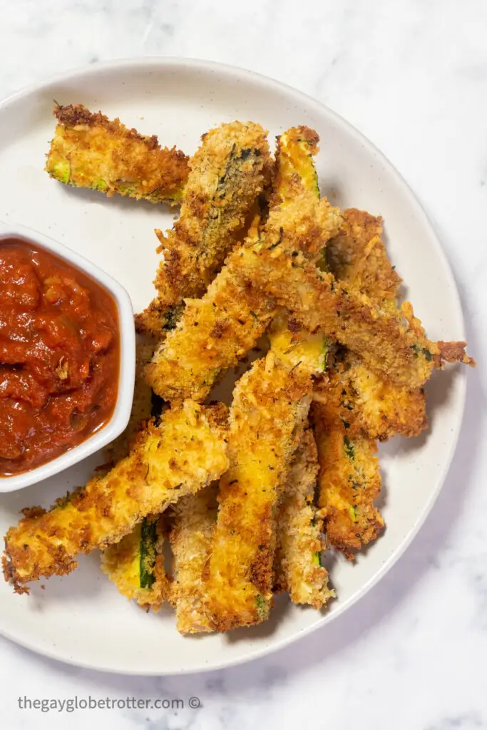 Air fryer zucchini fries on a plate next to marinara sauce.