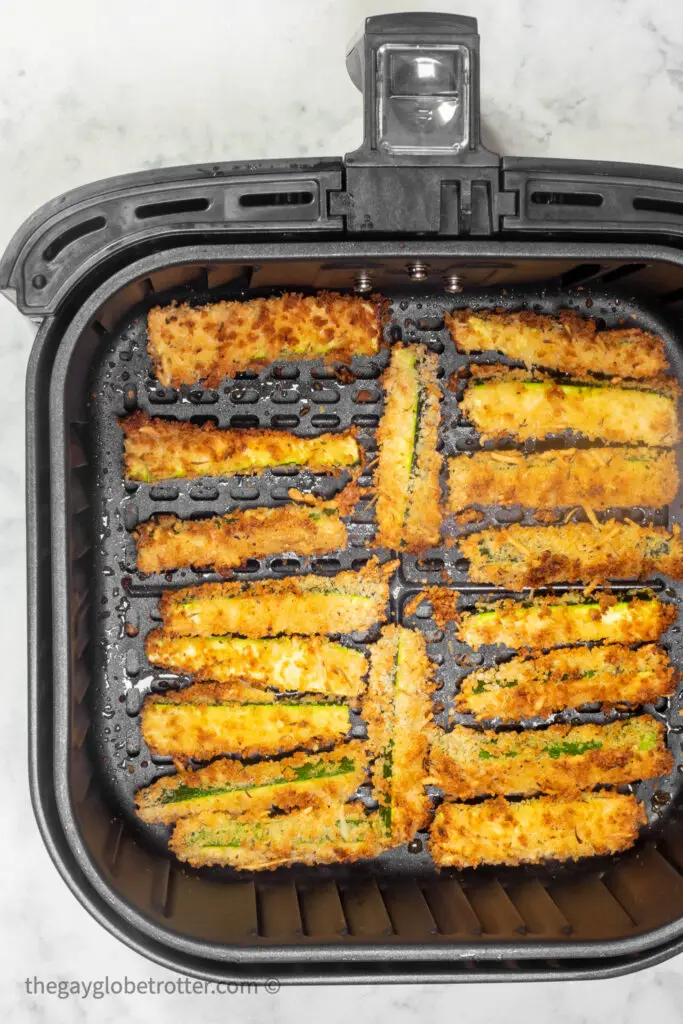 Cooked zucchini fries in an air fryer basket.