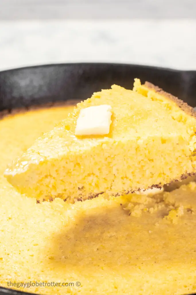 Cornbread topped with butter being served out of a cast iron skillet.