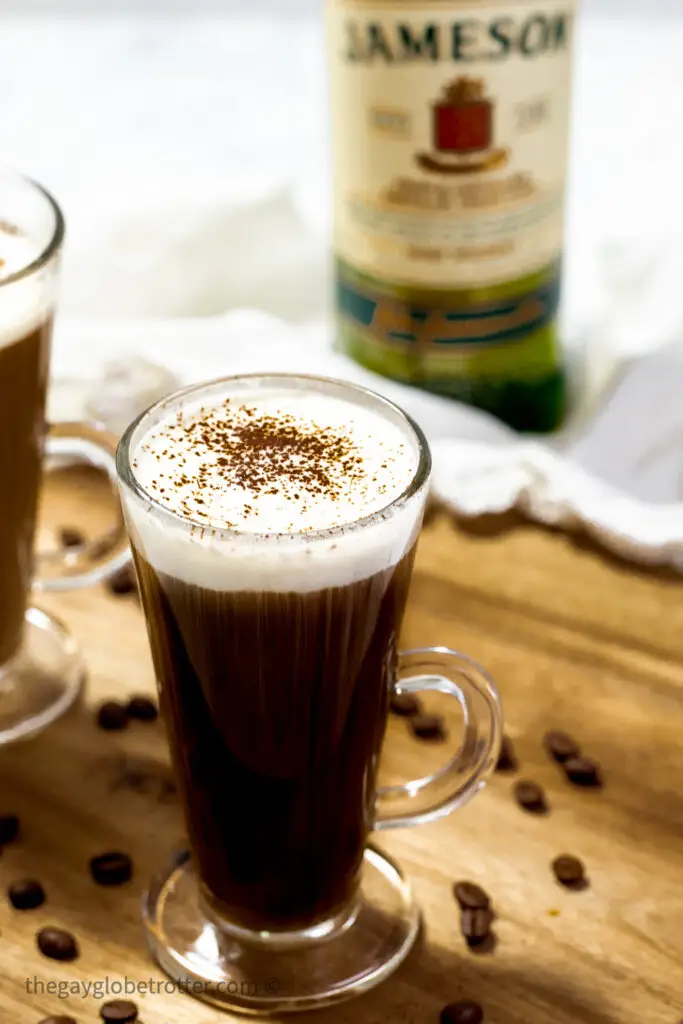 Irish coffee topped with powdered sugar next to coffee beans.