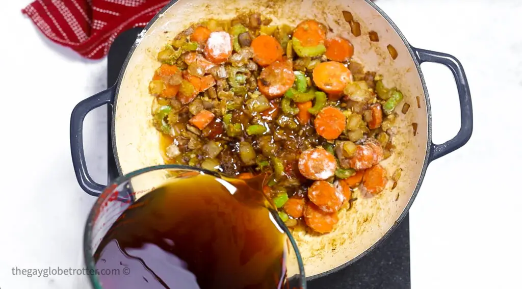 Beef broth being poured over stew vegetables.