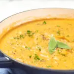 Root vegetable soup in a pot garnished with sage.