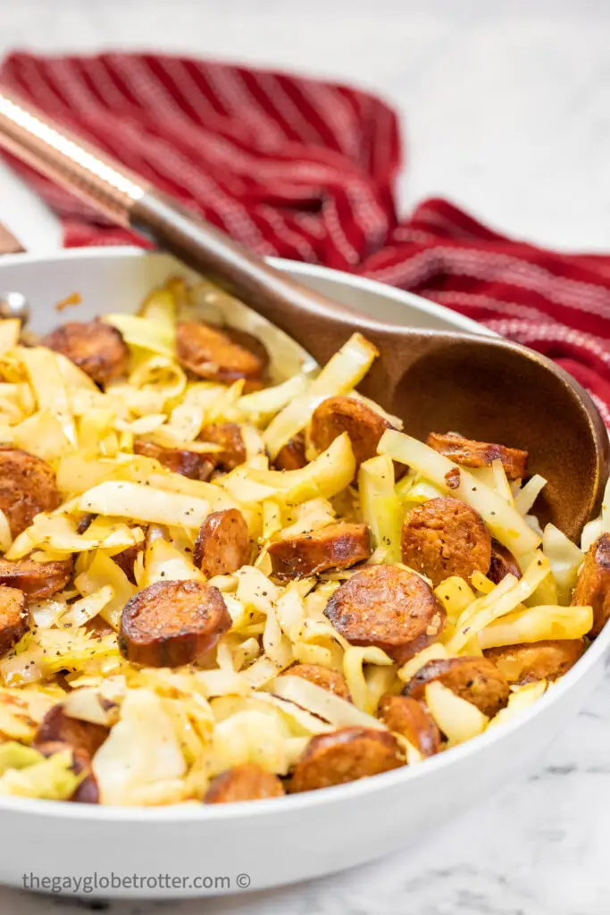 Cabbage and sausage in a skillet with a serving spoon.