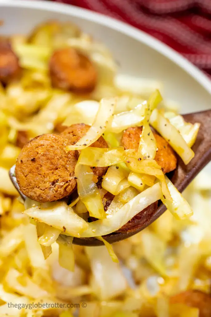 A spoon serving fried cabbage and sausage.