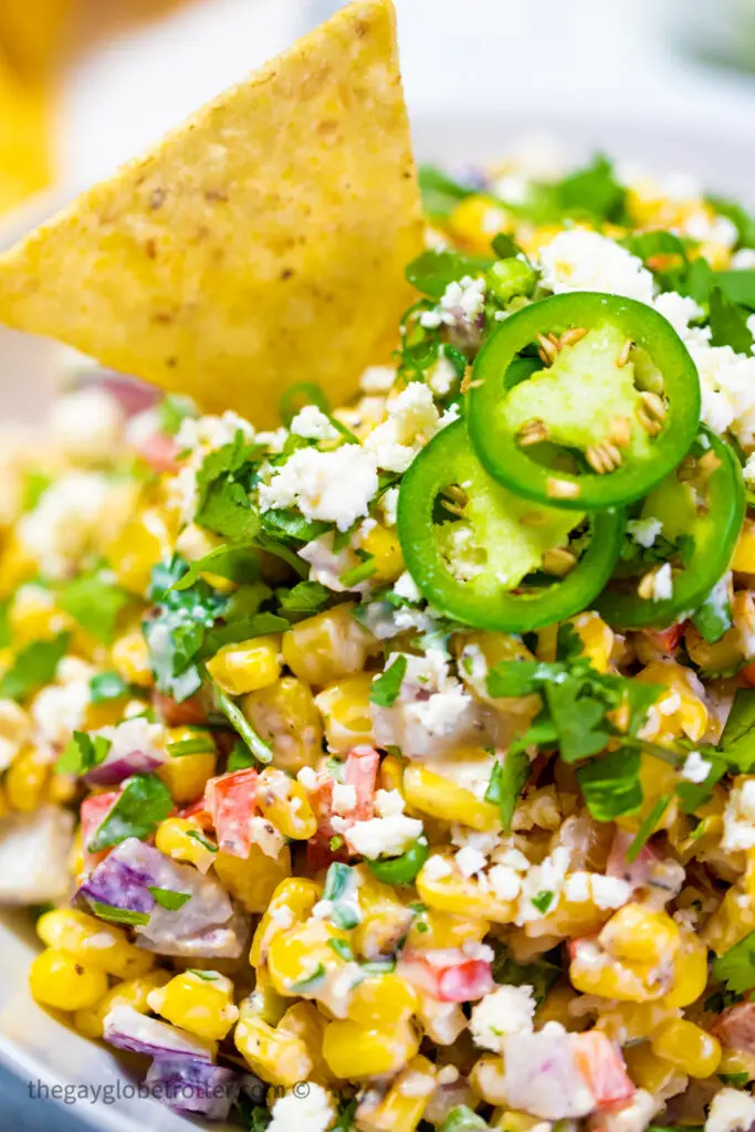 Mexican street corn dip garnished with a tortilla chip and jalapenos.