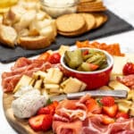 A charcuterie board next to crackers, crostini, and bread.