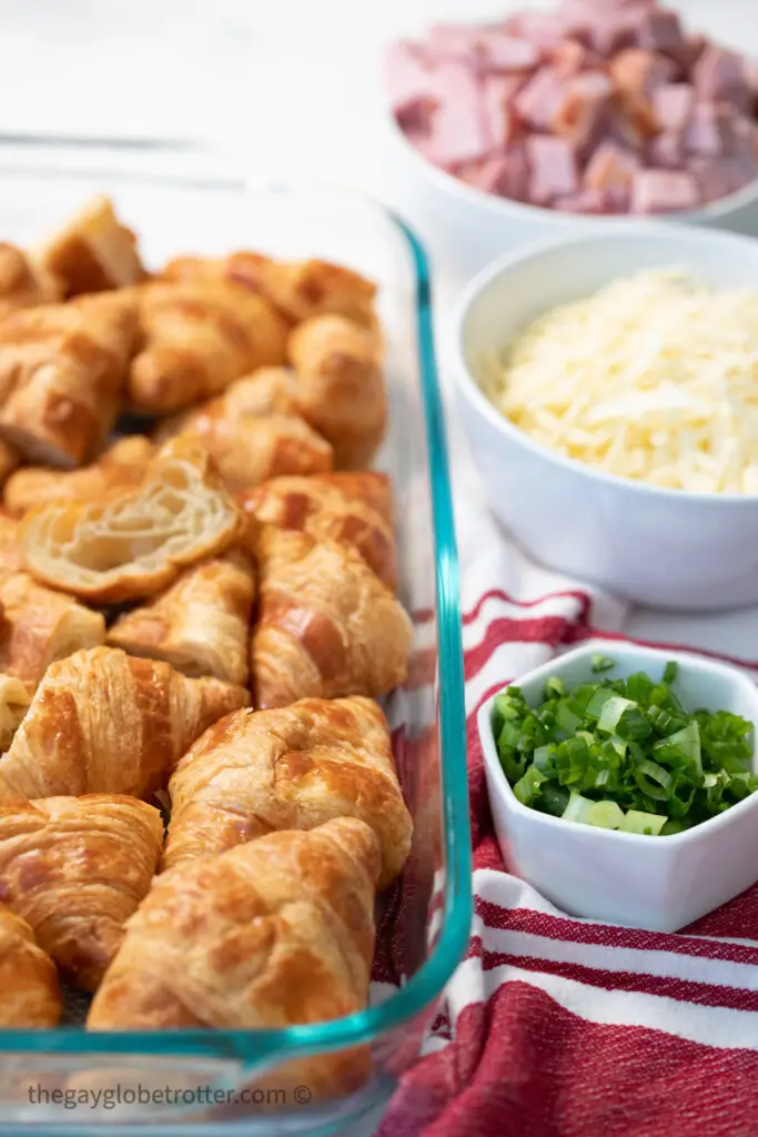 Croissants in a dish next to cubed ham, green onions, and cheese.