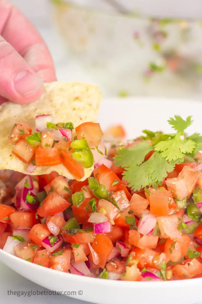 A tortilla chip scooping pico de gallo from a serving bowl.