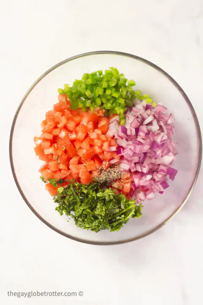 Tomatoes, red onions, jalapenos, and cilantro in a clear bowl.