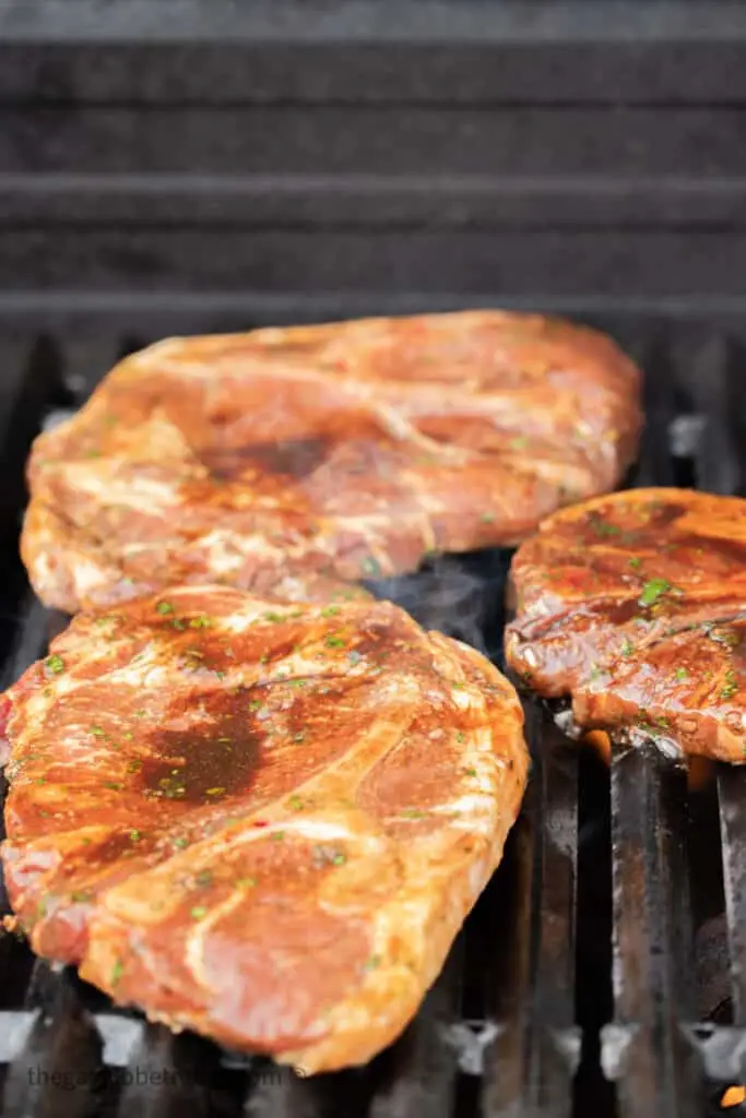 Three pork shoulder steaks on a grill.