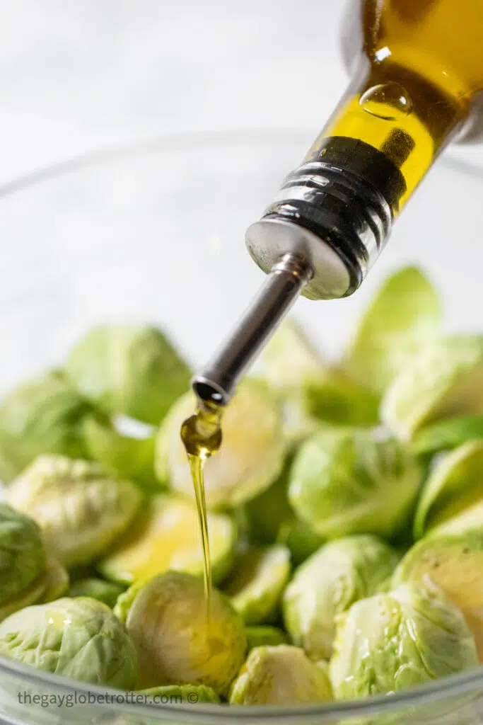 Olive oil being drizzled on a bowl of brussels sprouts.