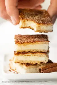 A hand picking up a churro cheesecake bar off of a pile.